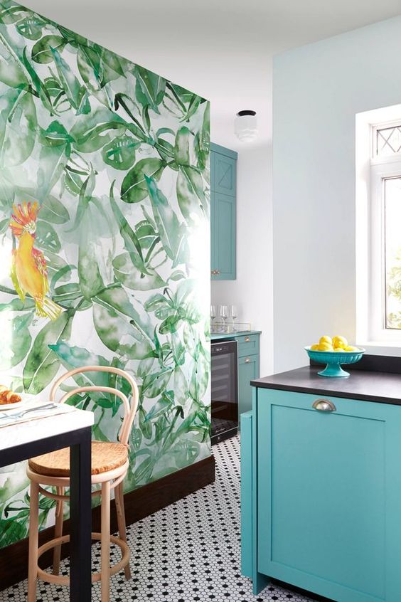 a bright tropical kitchen with blue cabinets, a mosaic tile wall, a tropical leaf statement wall, rattan stools