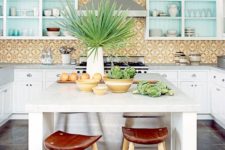 a bright tropical kitchen with yellow mosaic tiles, blue cabinets, tropical plants and leather and wood stools