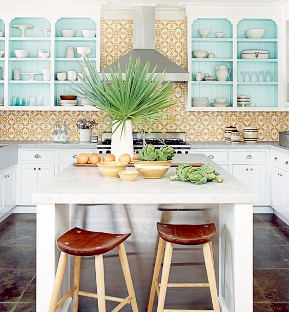a bright tropical kitchen with yellow mosaic tiles, blue cabinets, tropical plants and leather and wood stools