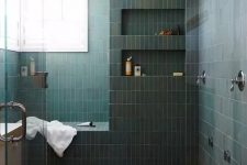 a chic bathroom with a large shower space clad with green stacked tiles, with a bench and niches in the walls, a dark-stained floor and windows for natural light