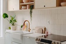 a chic kitchen in dove grey and light-colored plywood, with white countertops and a white skinny tile backsplash