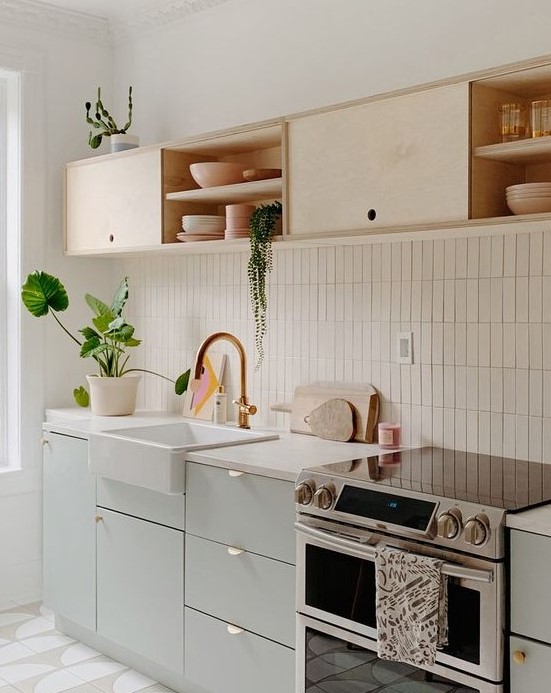 A chic kitchen in dove grey and light colored plywood, with white countertops and a white skinny tile backsplash