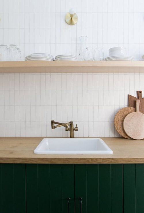 a chic modern kitchen with dark green cabinets, butcherblock countertops, an open shelf, a white skinny tile backsplash