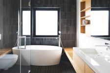 a contemporary bathroom all clad with matte dark skinny tiles and refreshed with light colored wood and white pieces