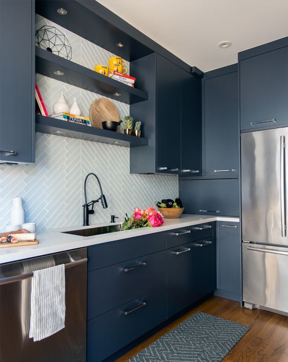 a contemporary blue kitchen with white countertops and a white tile backsplash clad with a pattern