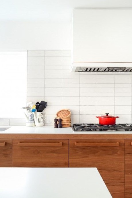 a contemporary wooden kitchen with a white hood, white countertops and a white stacked tile backsplash
