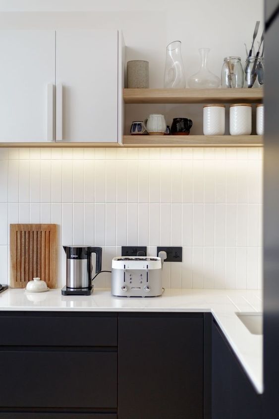 a contrasting black and white kitchen with white skinny tiles and white countertops, built-in lights and open shelves