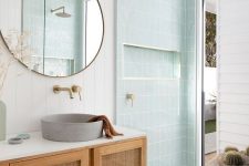 a dreamy mid-century modern bathroom with white and mint blue tiles, a rattan vanity, a round mirror and a round sink
