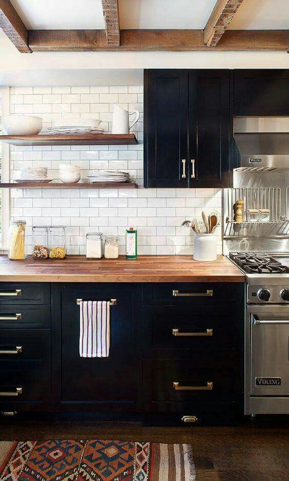 a farmhouse kitchen with black cabinets, neutral butcherblock countertops and brass hardware