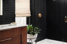 a mid-century modern bathroom with black skinny and white hex tiles, a stained vanity, a shower space, brass fixtures and potted plants