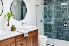 a mid-century modern bathroom with blue skinny tiles in the shower, white hex tiles on the floor, a stained vanity and round mirrors