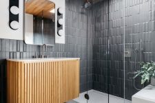a mid-century modern bathroom with graphite grey tiles, a fluted floating vanity, a shower space with a skylight