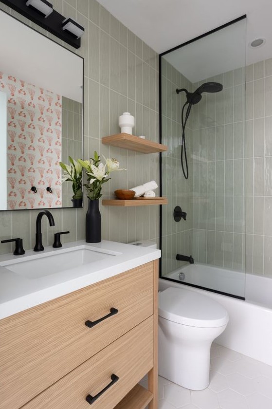 A mid century modern bathroom with grey skinny tiles, a timber vanity and shelves, black fixtures and white appliances