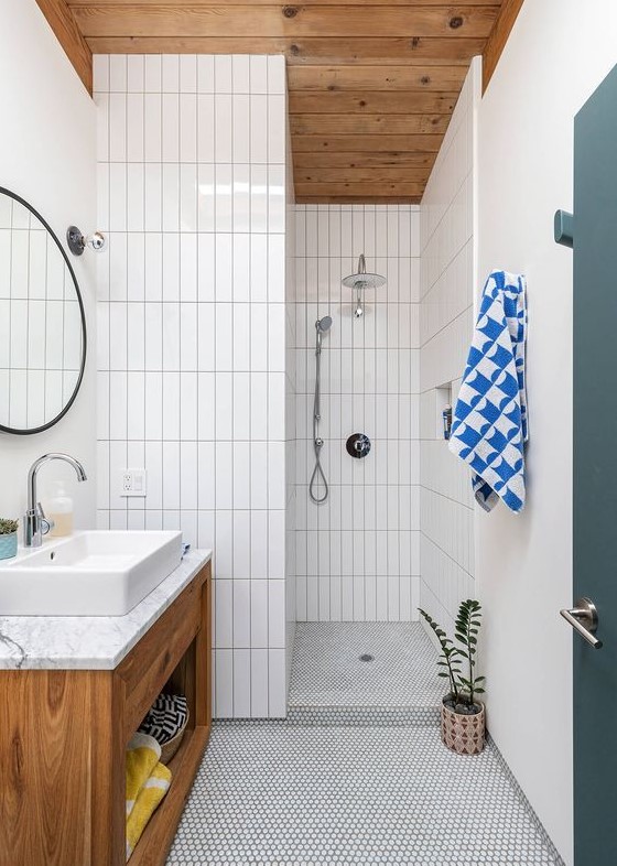 A mid century modern bathroom with stacked skinny tiles and penny ones, a stained vanity, a round mirror and a potted plat
