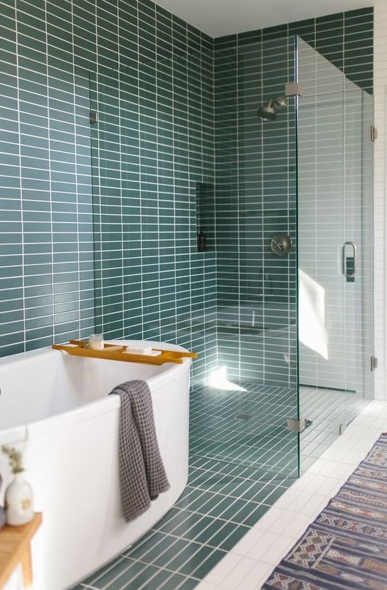 A mid century modern bathroom with teal skinny tiles, a white tub and a printed rug is a very welcoming space