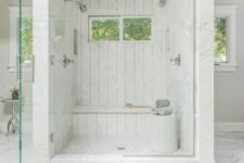 a mini marble shower space with windows and a built-in bench plus a side table with towels