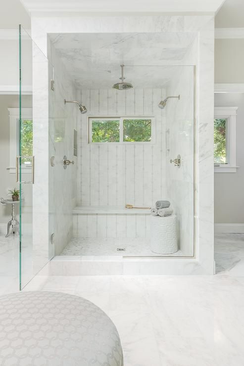 A mini marble shower space with windows and a built in bench plus a side table with towels