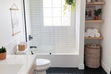 a modern farmhouse bathroom with an arched niche and built-in shelves, black herringbone and white skinny tiles, a timber vanity and some decor