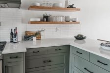 a modern farmhouse green kitchen with shaker cabinets, a white skinny tile backsplash and open shelves plus black sconces