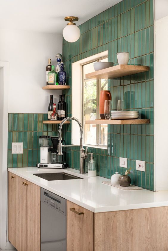 a modern kitchen with stained cabinets, a green skinny tile backsplash, white countertops and a sphere ceiling lamp