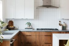 a modern stained and white kitchen with sleek cabinets, stone countertops, a white skinny tile backsplash and a metal hood
