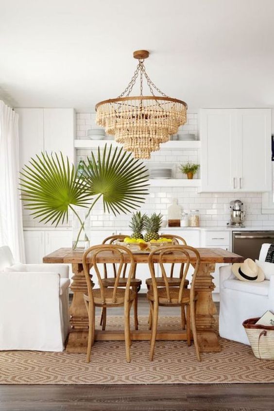 a modern kitchen in white, with a subway tile backsplash, a wooden bead chandelier, a wooden dining table and rattan chairs