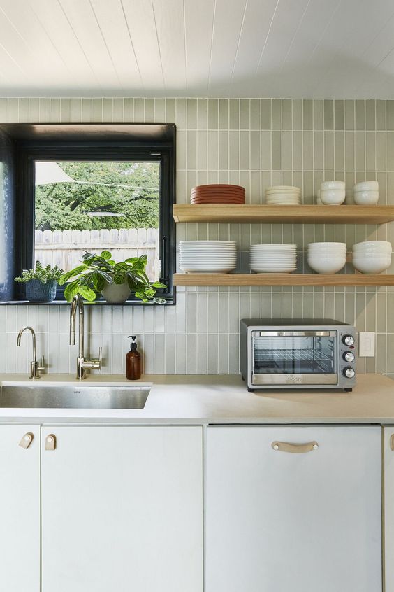 a modern white kitchen with a black frame window, a green skinny tile backsplash, open shelves and leather handles