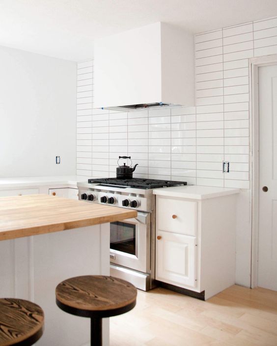 a modern white kitchen with shaker cabinets, a white skinny tile wall, a kitchen island with butcherblock countertops
