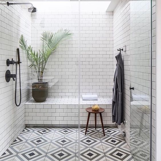 A monochromatic shower space with white subway tiles and a tiled built in bench plus mosaic floors