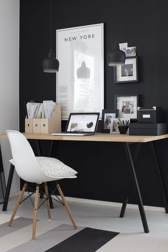 a moody home office with a black statement wall, pendant lamps, a desk with black legs and black framed artworks