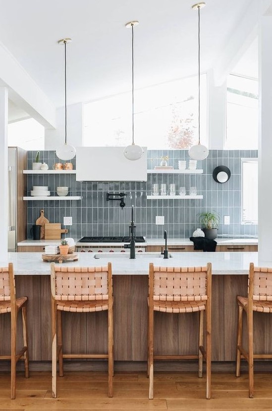 a neutral stained wooden kitchen, white shelves and a hood, a blue skinny tile wall and pendant lamps