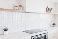 a pure white kitchen with sleek cabinets, open shelves, a hood and a white skinny tile backsplash with some decor