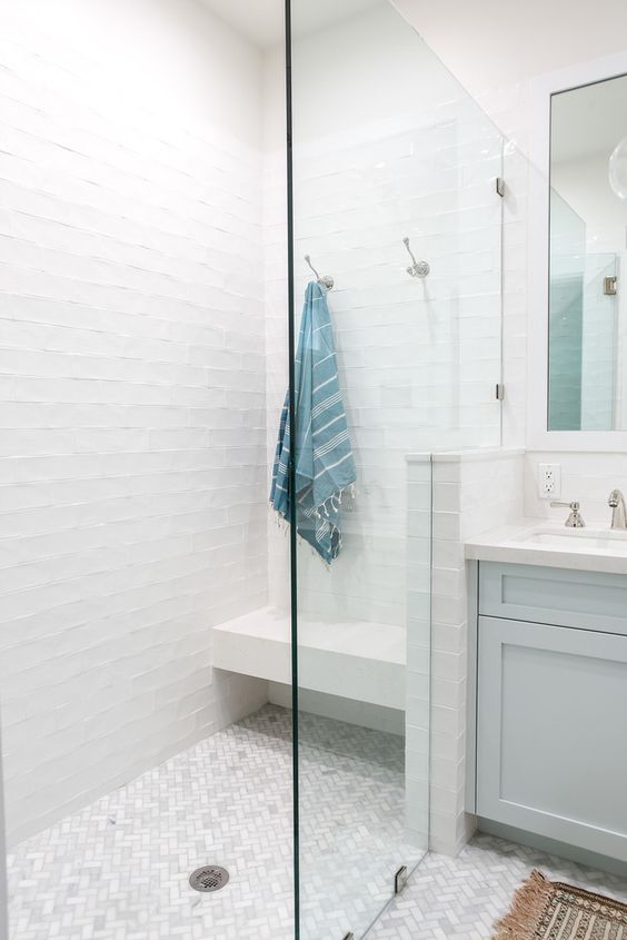 a pure white shower space with a floating bench and a marble tile floor plus seamless glass doors looks ethereal