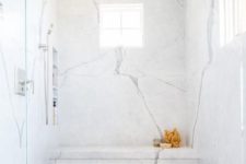 a refiend shower with thin gray marble herringbone floor tiles, marble slab walls featuring stacked shower niches and a marble shower bench