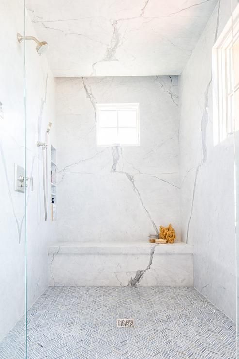 a refiend shower with thin gray marble herringbone floor tiles, marble slab walls featuring stacked shower niches and a marble shower bench