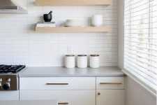 a serene white kitchen with a skinny tile wall, creamy cabinets, open shelves and brass fixtures for more chic