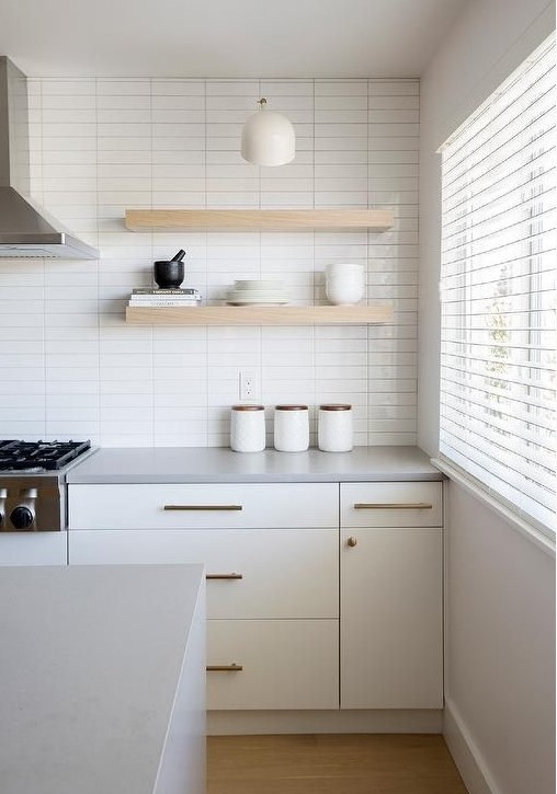 a serene white kitchen with a skinny tile wall, creamy cabinets, open shelves and brass fixtures for more chic