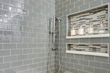 a shiny grey tile shower space with a built-in bench with a white seat and some catchy niches in the wall