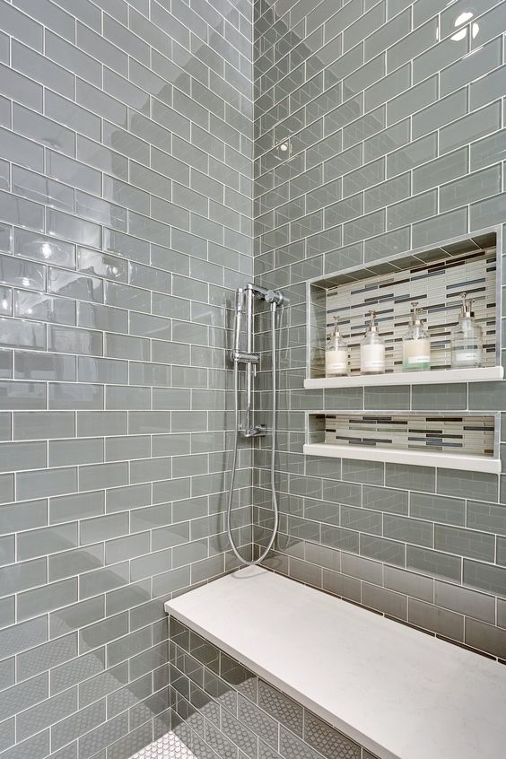 a shiny grey tile shower space with a built-in bench with a white seat and some catchy niches in the wall