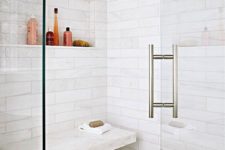 a shower space done with white marble tiles, smaller ones on the floor and a marble floating bench