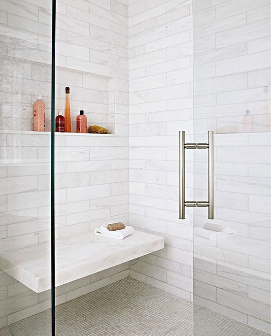 a shower space done with white marble tiles, smaller ones on the floor and a marble floating bench