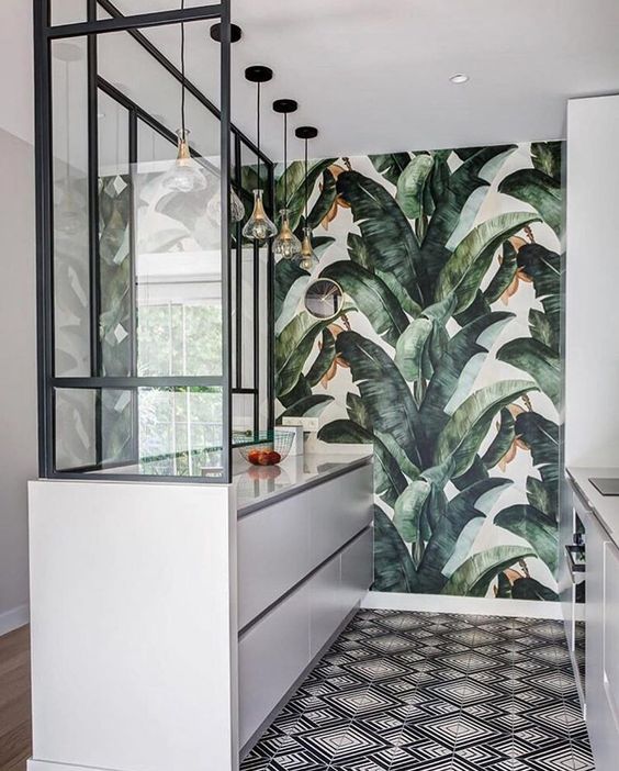 a small and minimalist tropical kitchen with sleek white cabinets, a mosaic floor and a torpical leaf statement wall and pendant lamps