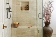 a small and welcoming earthy shower space with a built-in bench, dark hardware and tiles for a touch of drama