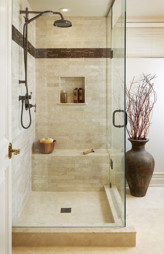 a small and welcoming earthy shower space with a built-in bench, dark hardware and tiles for a touch of drama