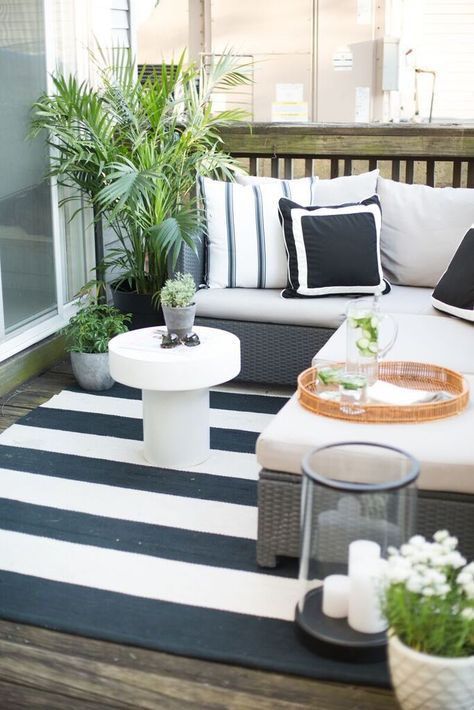 A small black and white deck with an L shaped upholstered bench, a coffee table, a candle lantern and potted greenery