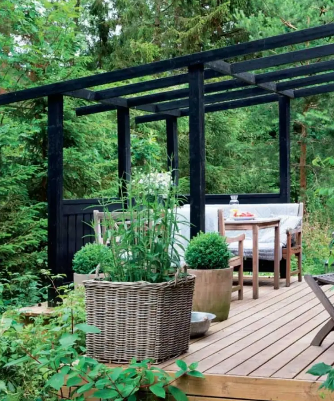 a small deck with a roof over it to hang curtains, a comfortable dining space with simpel wooden furniture and potted greenery
