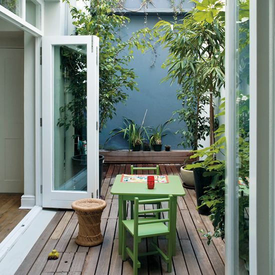 a small deck with green furniture, potted greenery and a rattan side table feels very welcoming and secluded