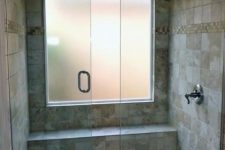 a small earthy-colored shower space with tiles of various scales and a frosted glass window plus a narrow built-in bench