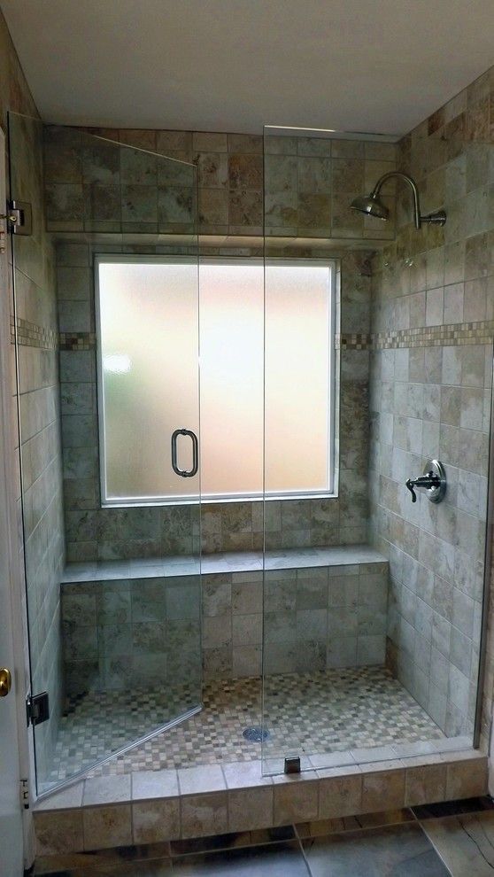 A small earthy colored shower space with tiles of various scales and a frosted glass window plus a narrow built in bench
