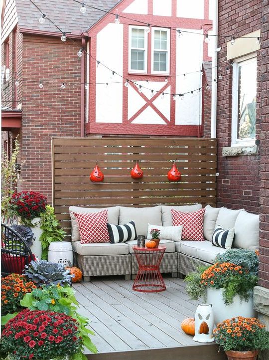 A small fall inspired deck with an L shaped upholstered bench, colorful pillows and potted blooms